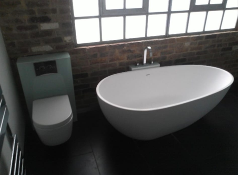 Freestanding oval bathtub and wall-hung toilet against a brick feature wall, bathroom installation, London.