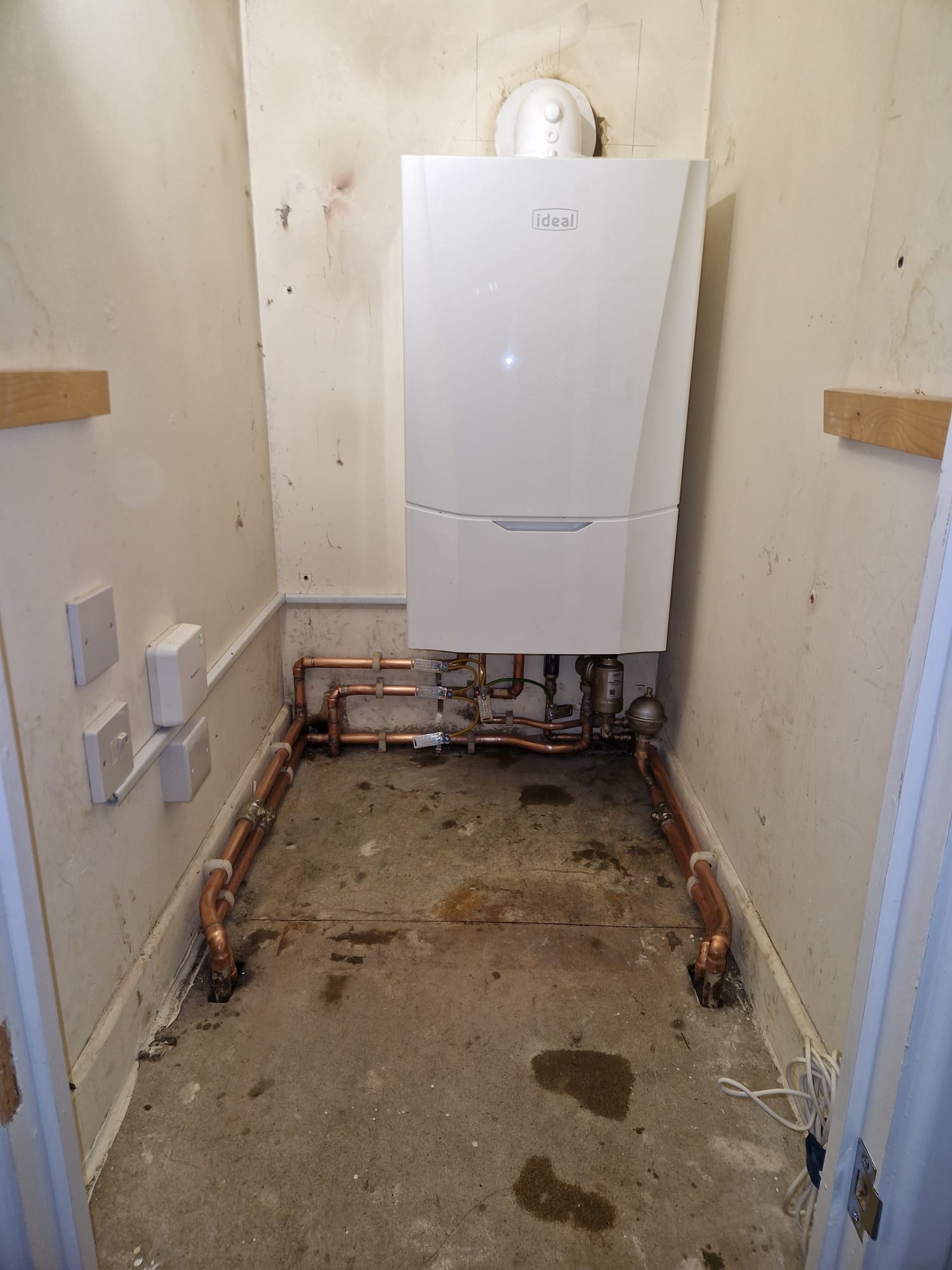 Ideal boiler installed in a wide alcove with structured copper pipework across the floor.